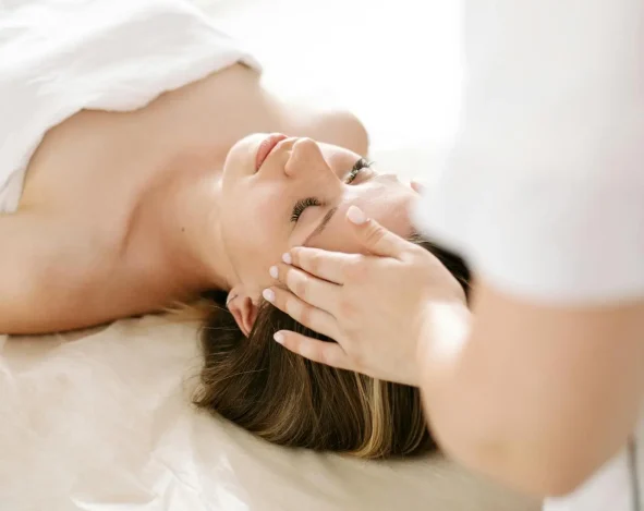 Reiki therapist gently resting hands on a client’s head in a peaceful treatment room.
